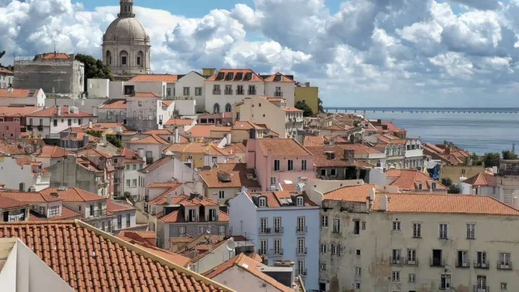 Vista panorâmica dos telhados vermelhos e fachadas coloridas do bairro Alfama em Lisboa com o Panteão Nacional ao fundo