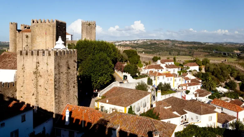 Vista panorâmica do Castelo de Óbidos e muralhas medievais com casario branco típico em um dia ensolarado.