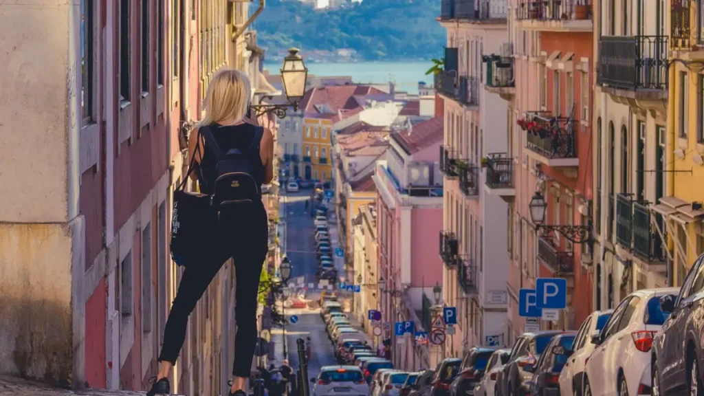 Mulher de costas com mochila observando ladeira íngreme em Lisboa com vista para o Rio Tejo