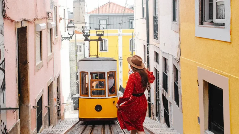 Mulher caminhando sozinha em ladeira com ascensor amarelo da Bica em Lisboa em guia de transporte público