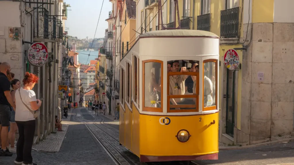 Tradicional Ascensor da Bica amarelo descendo rua histórica de Lisboa em dia ensolarado