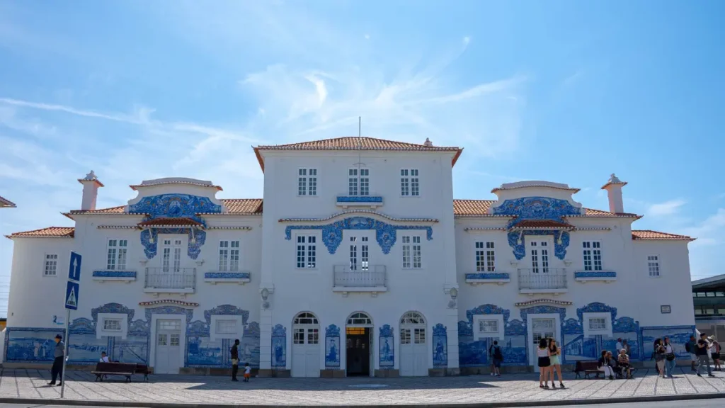 Fachada branca da Estação de Trem de Aveiro decorada com painéis de azulejos azuis e amarelos sob céu limpo.