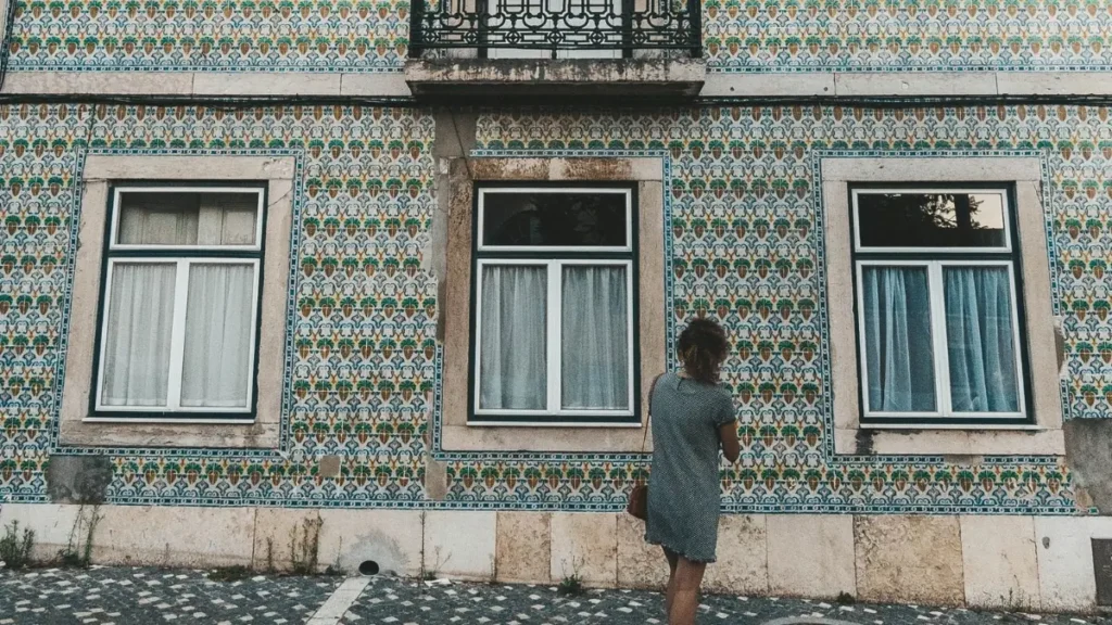 Mulher caminhando sozinha observando fachada de prédio histórico coberta de azulejos tradicionais em Lisboa