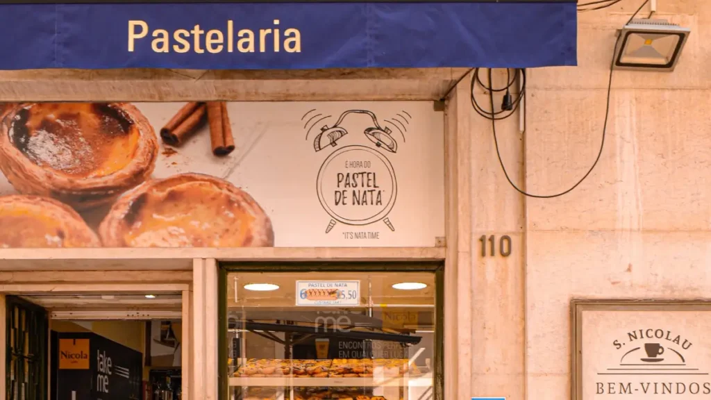 Fachada da Pastelaria S. Nicolau em Lisboa com vitrine cheia de pasteis de nata e calcada portuguesa