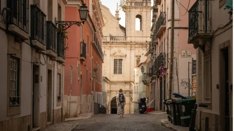 Mulher caminhando sozinha de costas em ruela histórica charmosa e segura de Portugal com igreja ao fundo