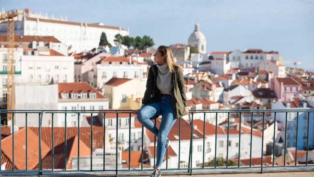 Mulher sentada no parapeito de um miradouro em Alfama observando os telhados históricos de Lisboa e o Panteão Nacional
