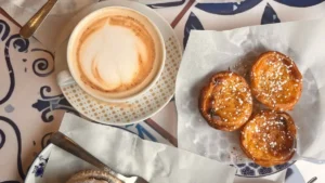 Mesa com azulejos portugueses servida com pasteis de nata polvilhados com canela e cafes espresso para guia o que comer em lisboa
