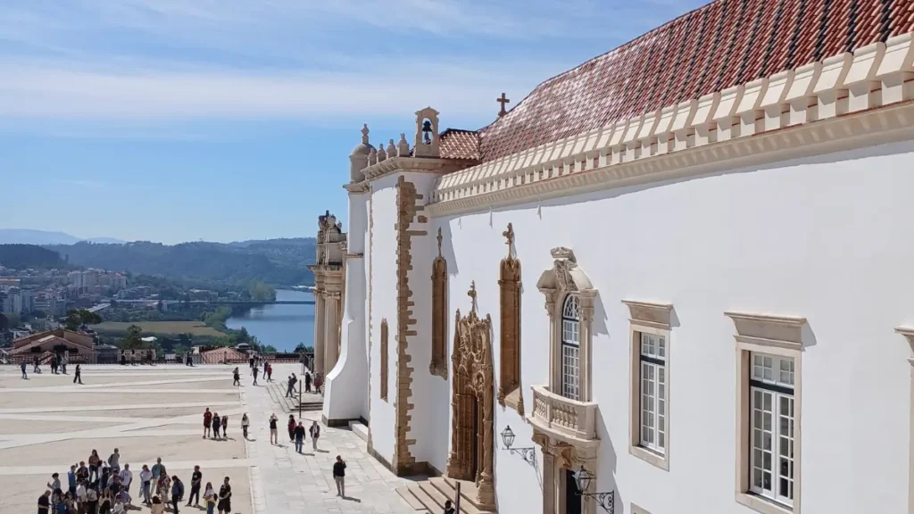Pátio do Paço das Escolas na Universidade de Coimbra com turistas e vista para o Rio Mondego.