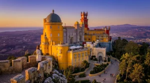 Viajante solo em um mirante de pedra contemplando a vista panorâmica do Palácio Nacional da Pena em Sintra durante o pôr do sol.