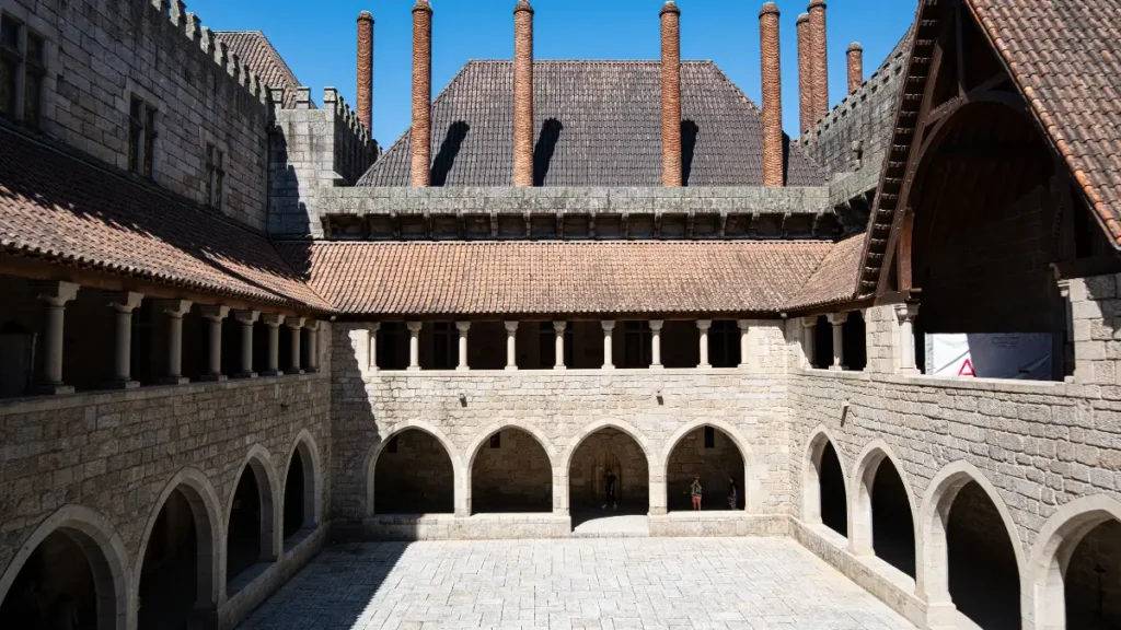 Pátio interno de pedra do Paço dos Duques de Bragança com arcos góticos e chaminés cilíndricas em Guimarães.