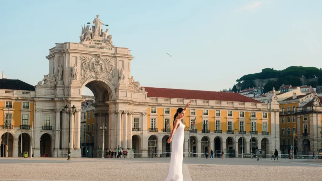 Mulher em vestido branco na Praça do Comércio em Lisboa com o monumento do Arco da Rua Augusta ao fundo.
