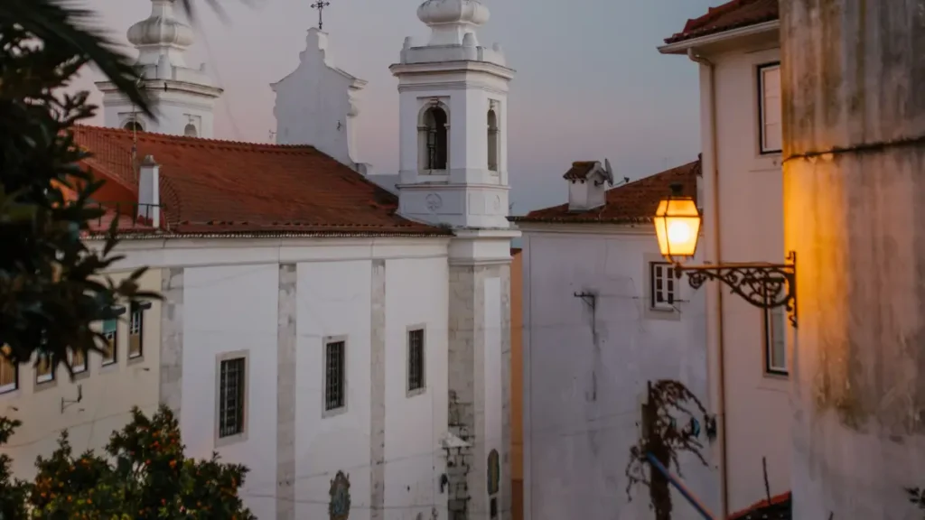 Escadaria tradicional de Alfama iluminada por lampião ao entardecer com igreja histórica ao fundo em Lisboa