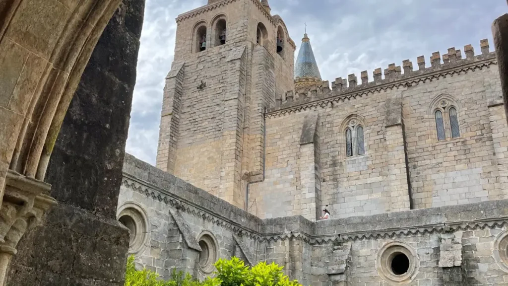 Claustro em pedra da Sé Catedral de Évora emoldurado por arco com jardim e laranjeiras.
