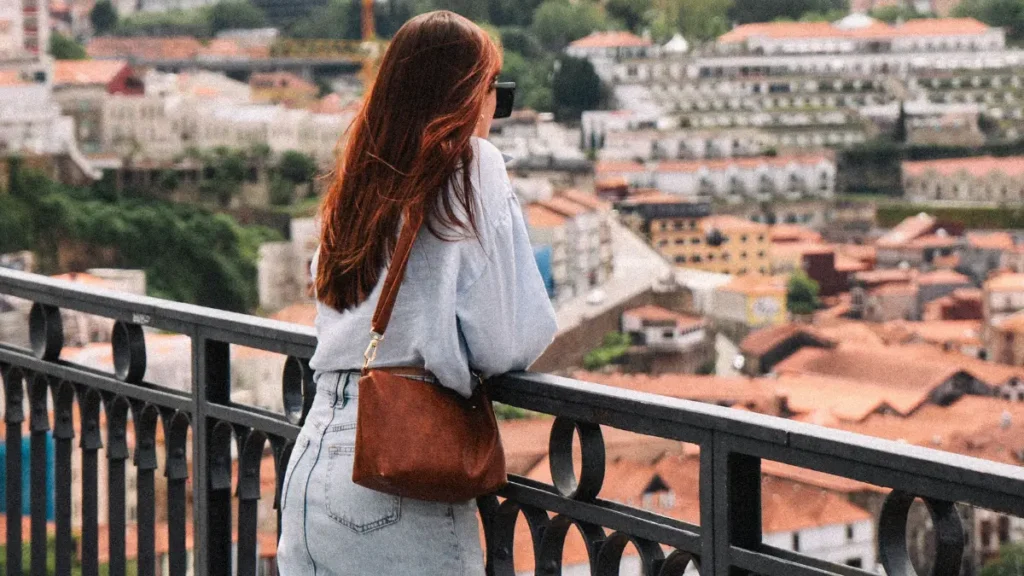 Mulher de cabelos ruivos e saia jeans longa contemplando a vista da cidade do Porto, Portugal, durante sua primeira viagem solo feminina aos 40.