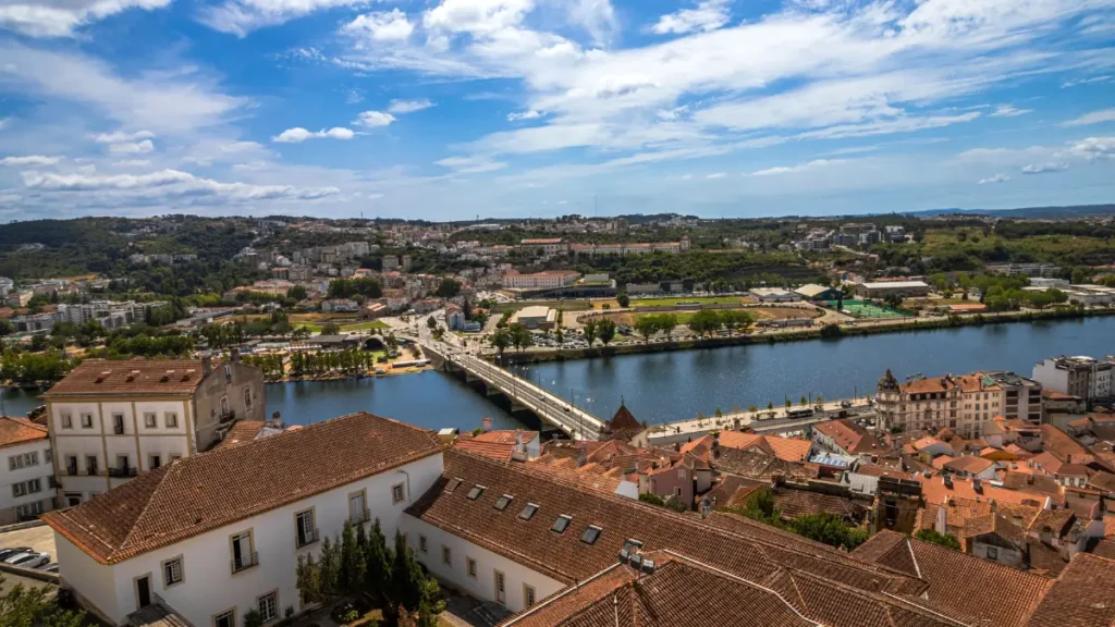 Vista do topo de Coimbra mostrando os telhados vermelhos da Baixa, a ponte e o Rio Mondego.